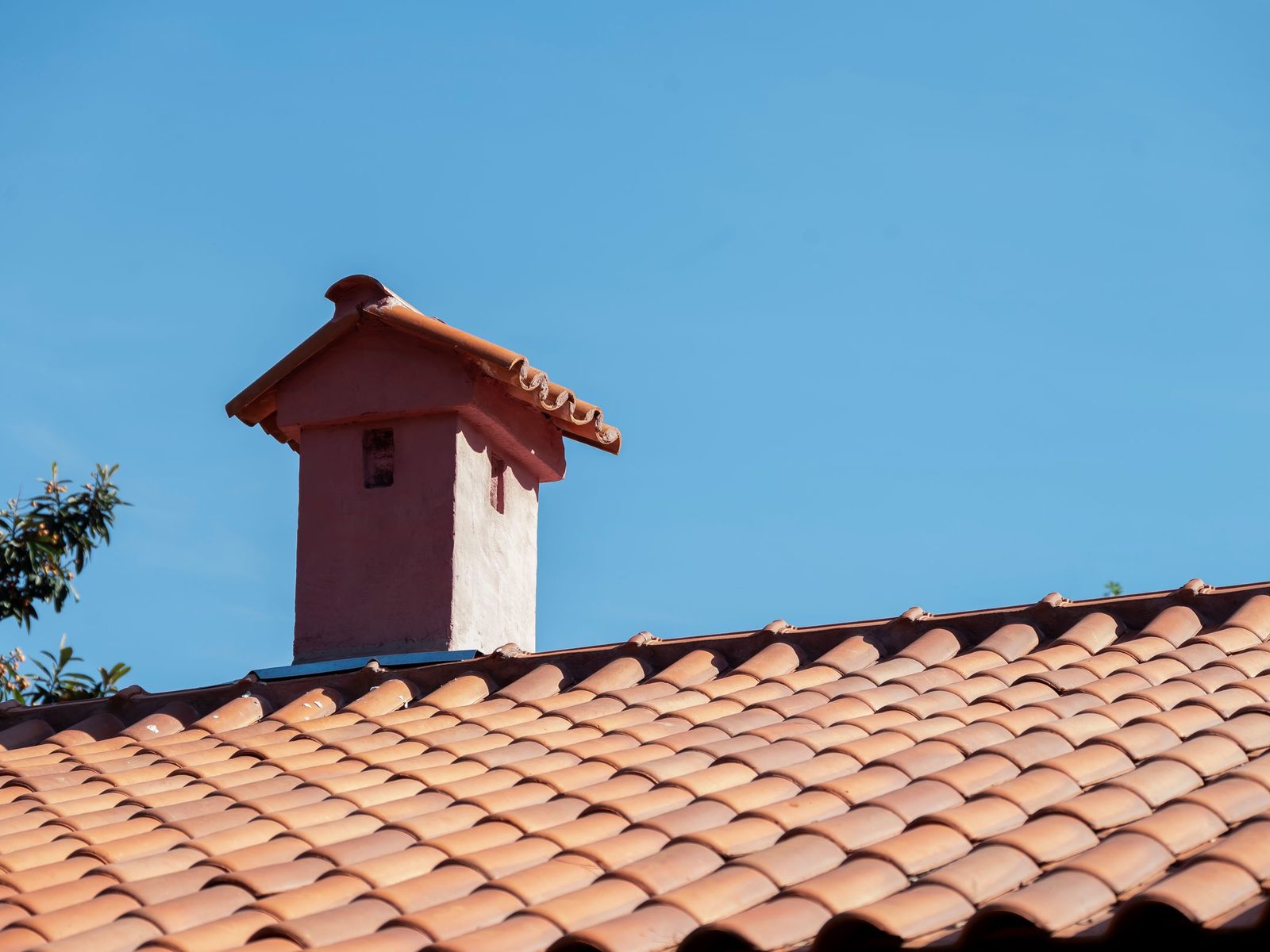 Pink stucco chimney on a clay tile roof against a blue sky